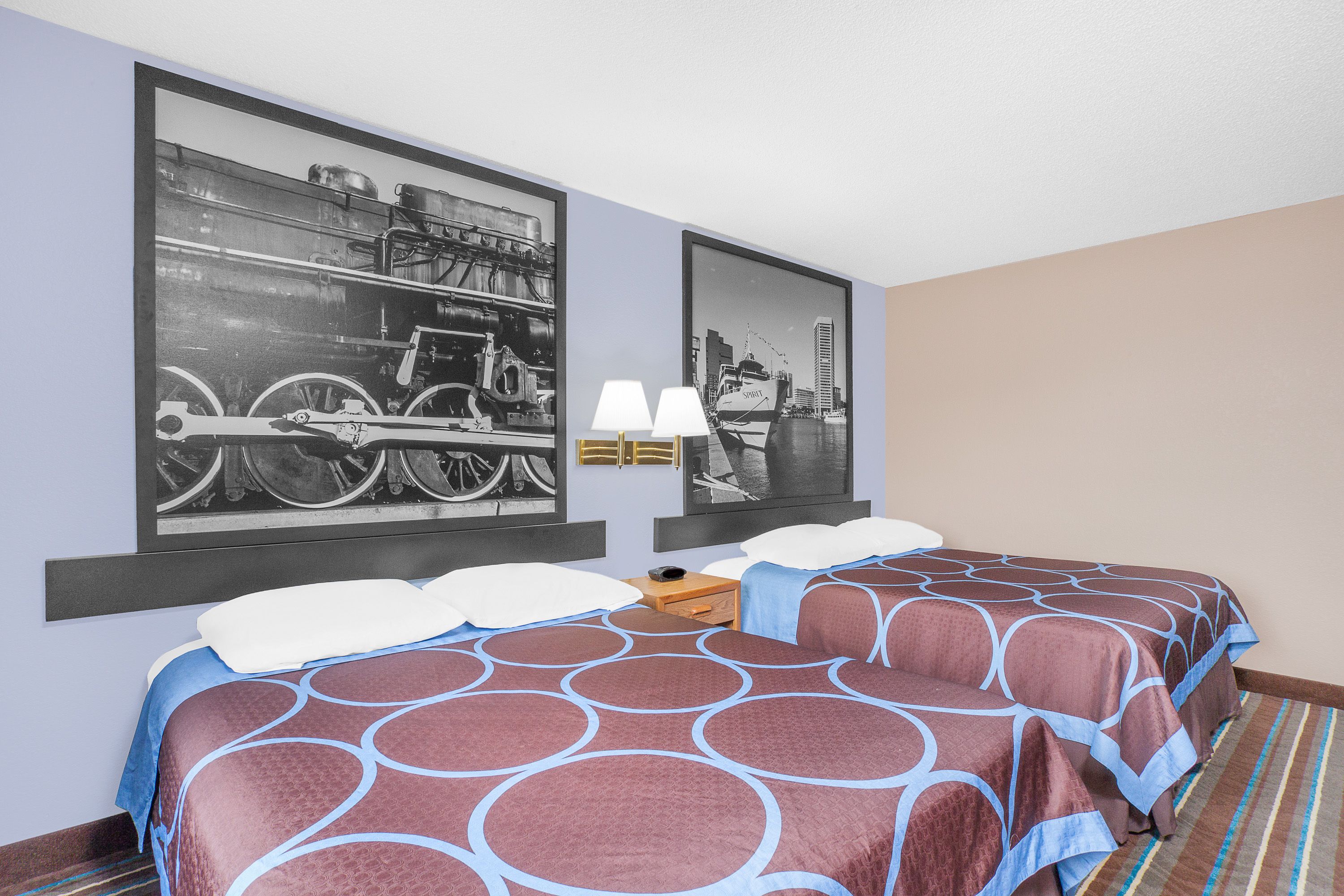 A hotel room with two beds, a cityscape artwork on the wall, a lamp, and a striped carpet.