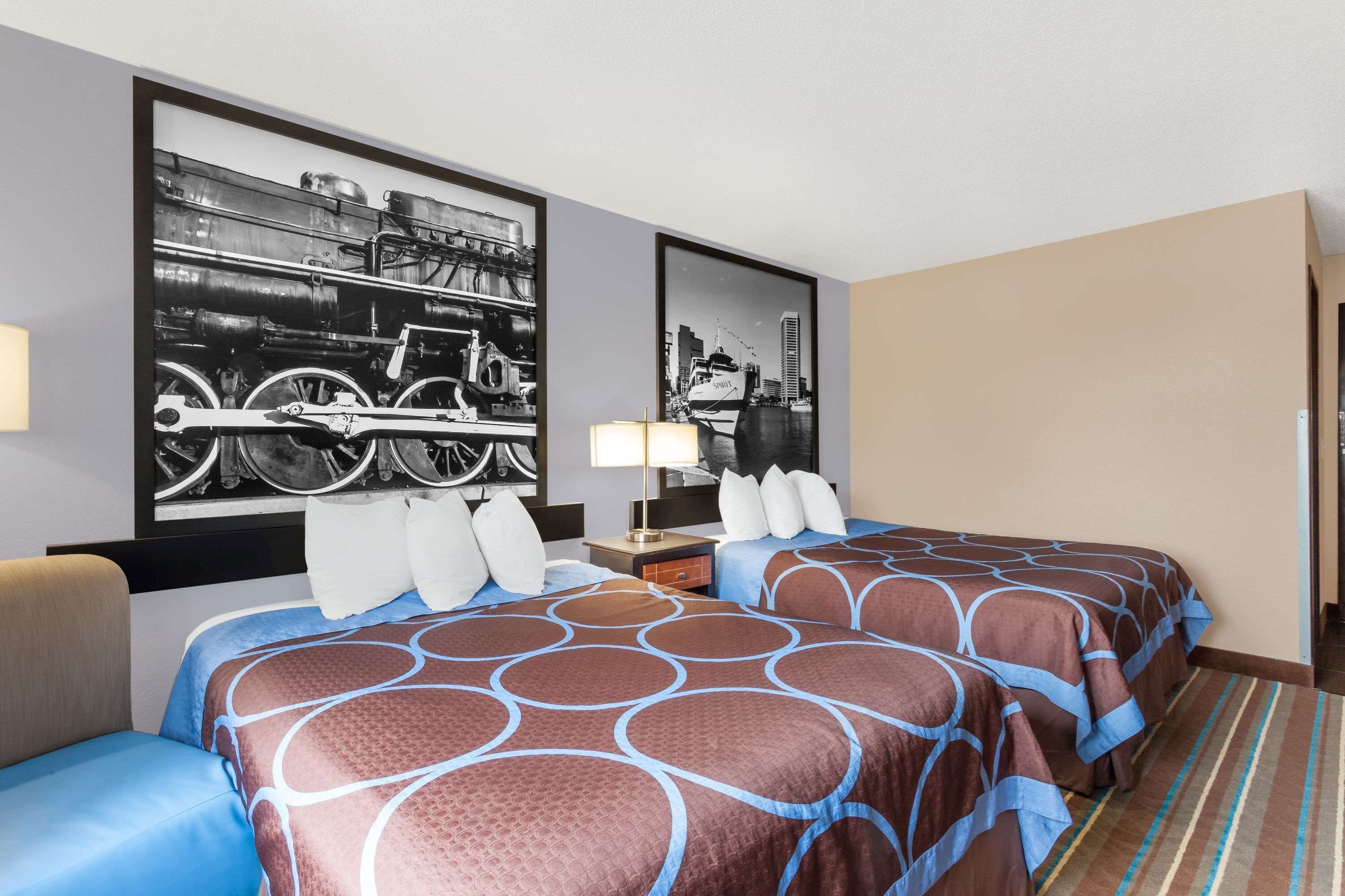A hotel room with two beds, a large black and white photo on the wall, a lamp, and a striped carpet.