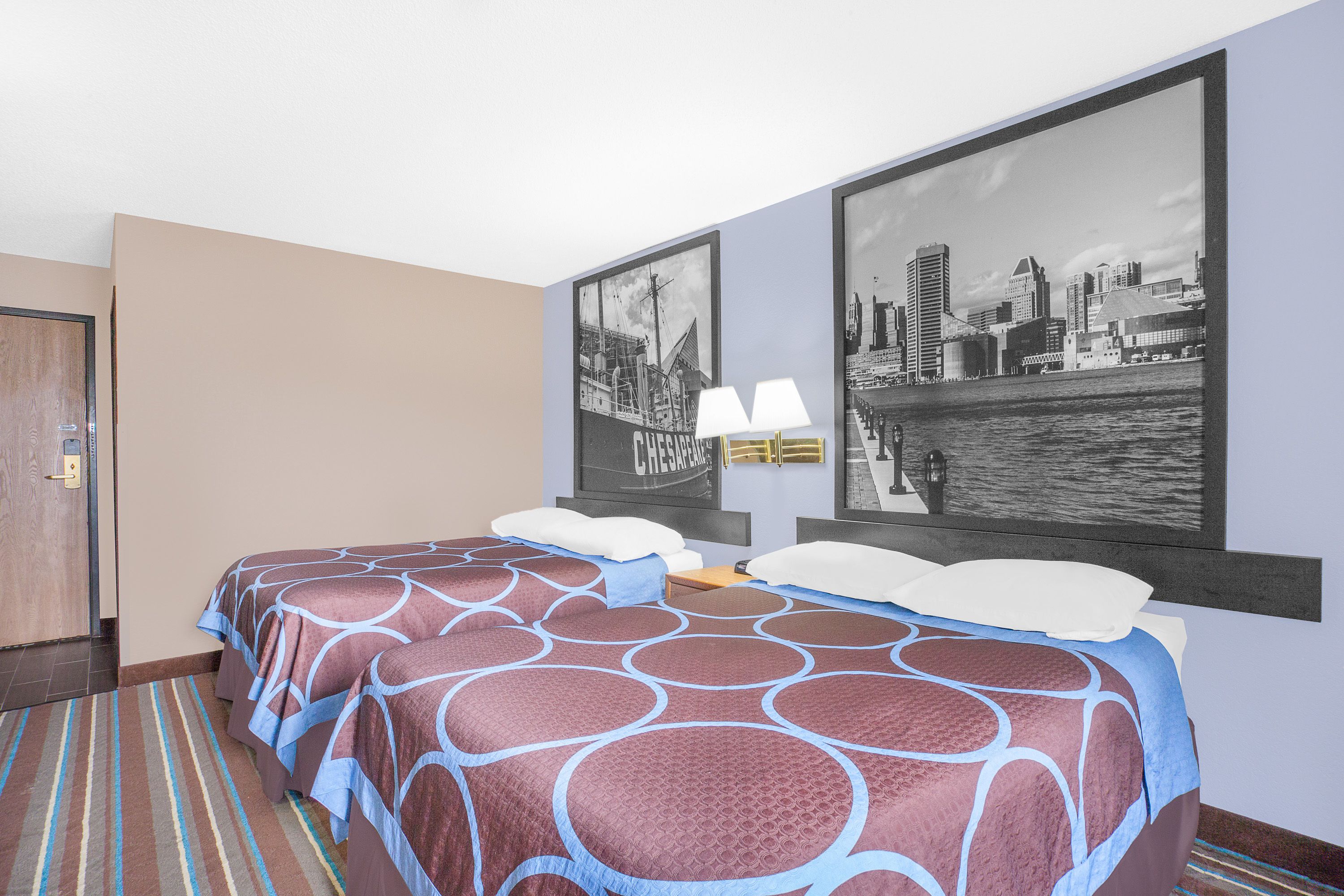 A hotel room with a large bed, a cityscape view, a door, and a striped carpet.