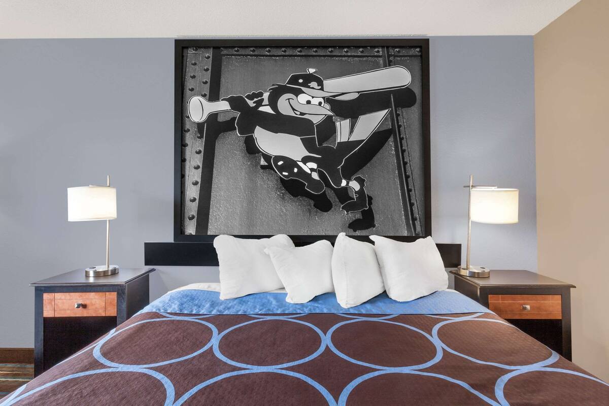 Quarto de hotel com uma cama, duas mesas de cabeceira, duas luminárias e um mural grande na parede.