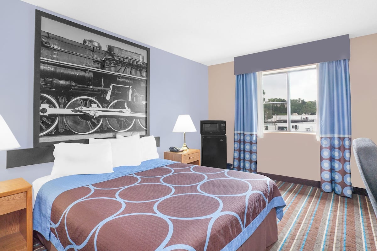 Quarto de hotel com uma cama grande, televisão, escrivaninha e janela com cortinas.