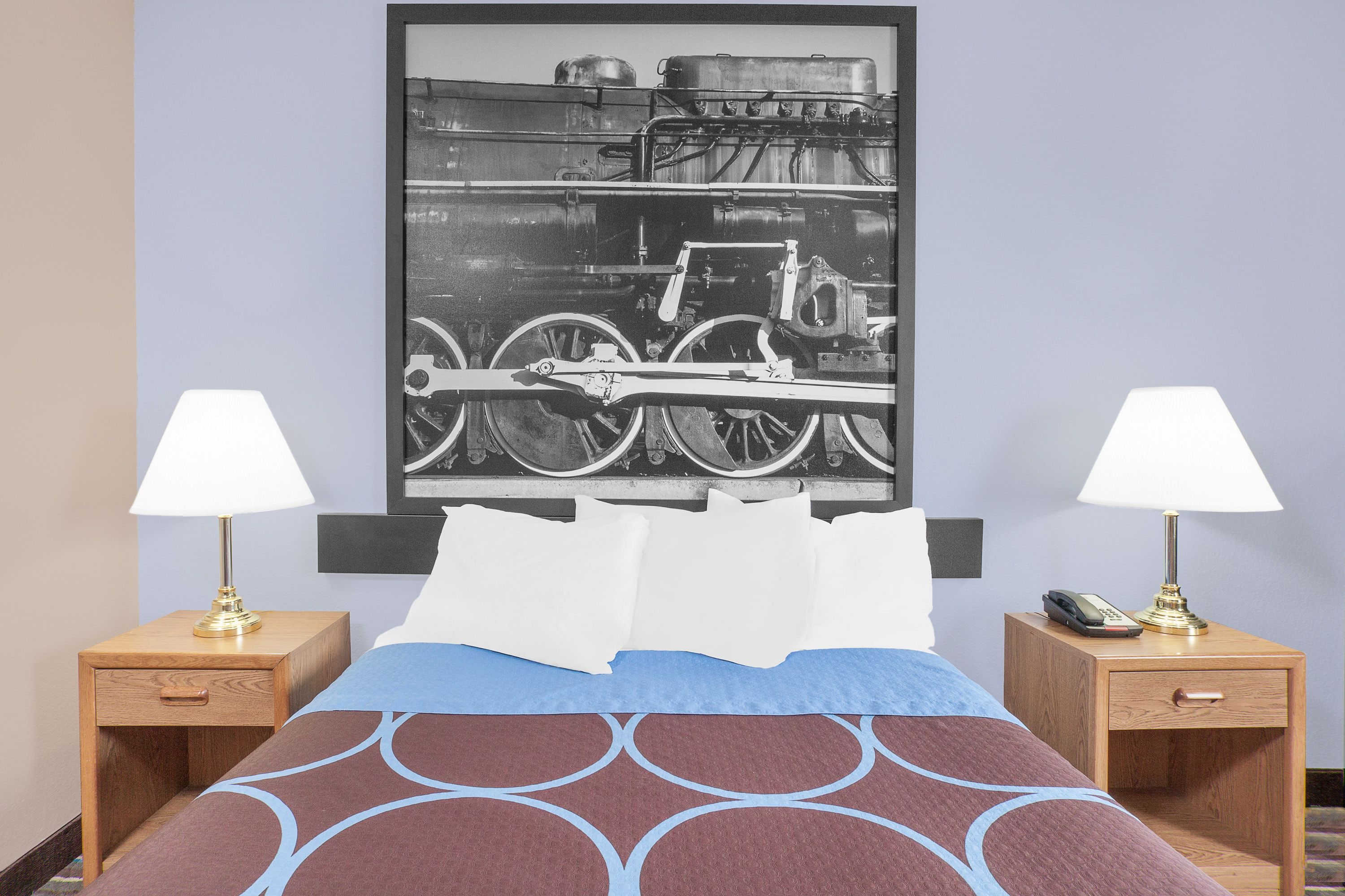 A hotel room with a bed, two nightstands with lamps, a framed picture on the wall, and a telephone on one of the nightstands.