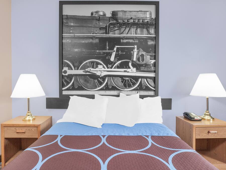 A hotel room with a bed, two nightstands with lamps, a framed picture on the wall, and a telephone on one of the nightstands.
