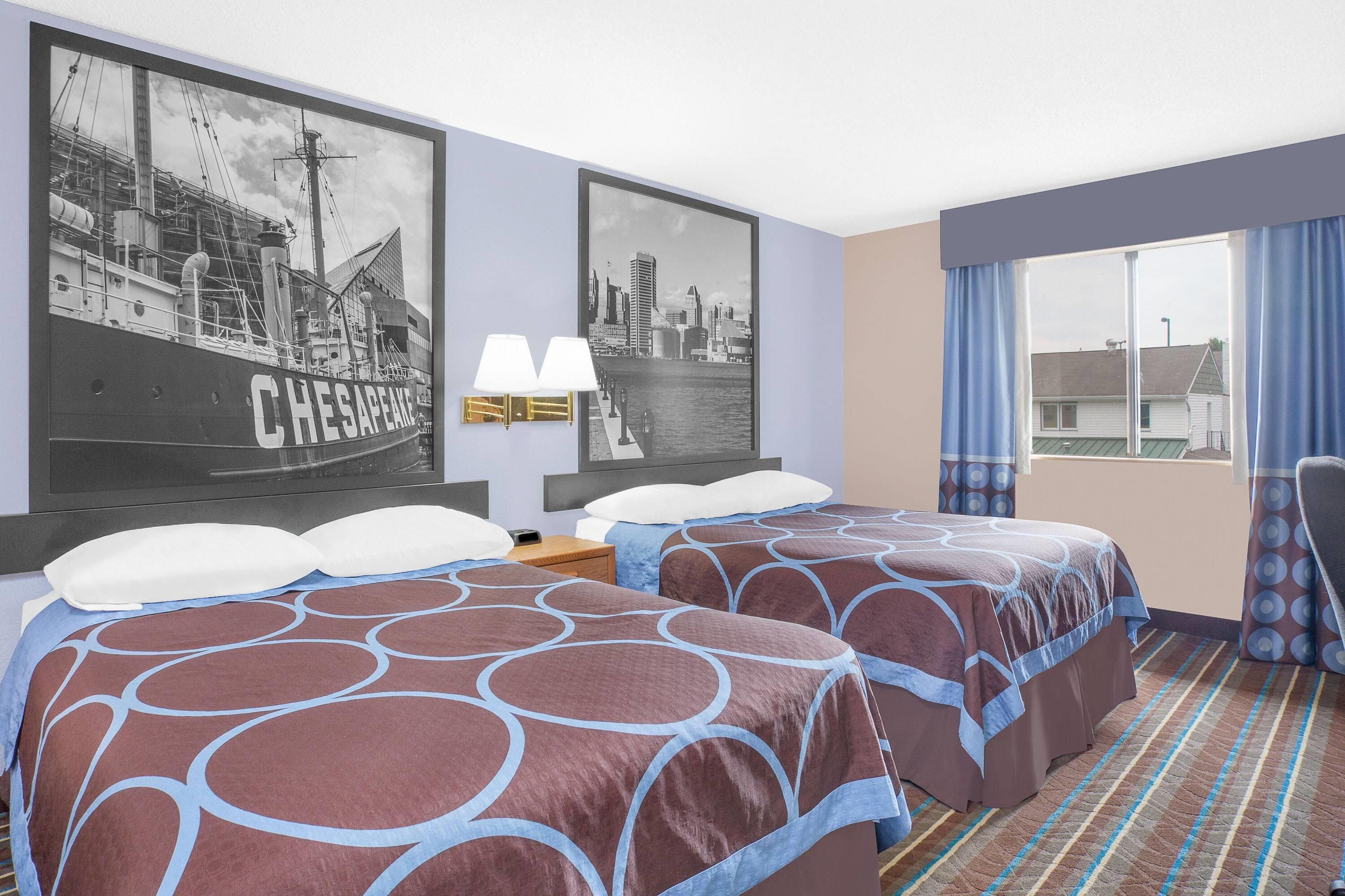 Habitación de hotel con dos camas, un cartel con un motivo urbano, una ventana con cortinas y vistas a edificios.