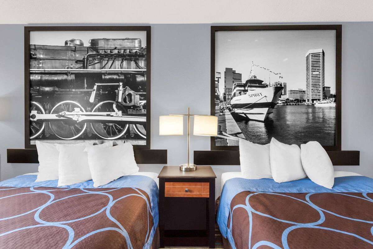 Quarto de hotel com duas camas, uma mesinha de cabeceira e duas luminárias fixadas na parede.