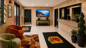Eine Hotelhalle mit Empfangsschalter, einem an der Wand befestigten Fernseher, einer Couch und Zimmerpflanzen.