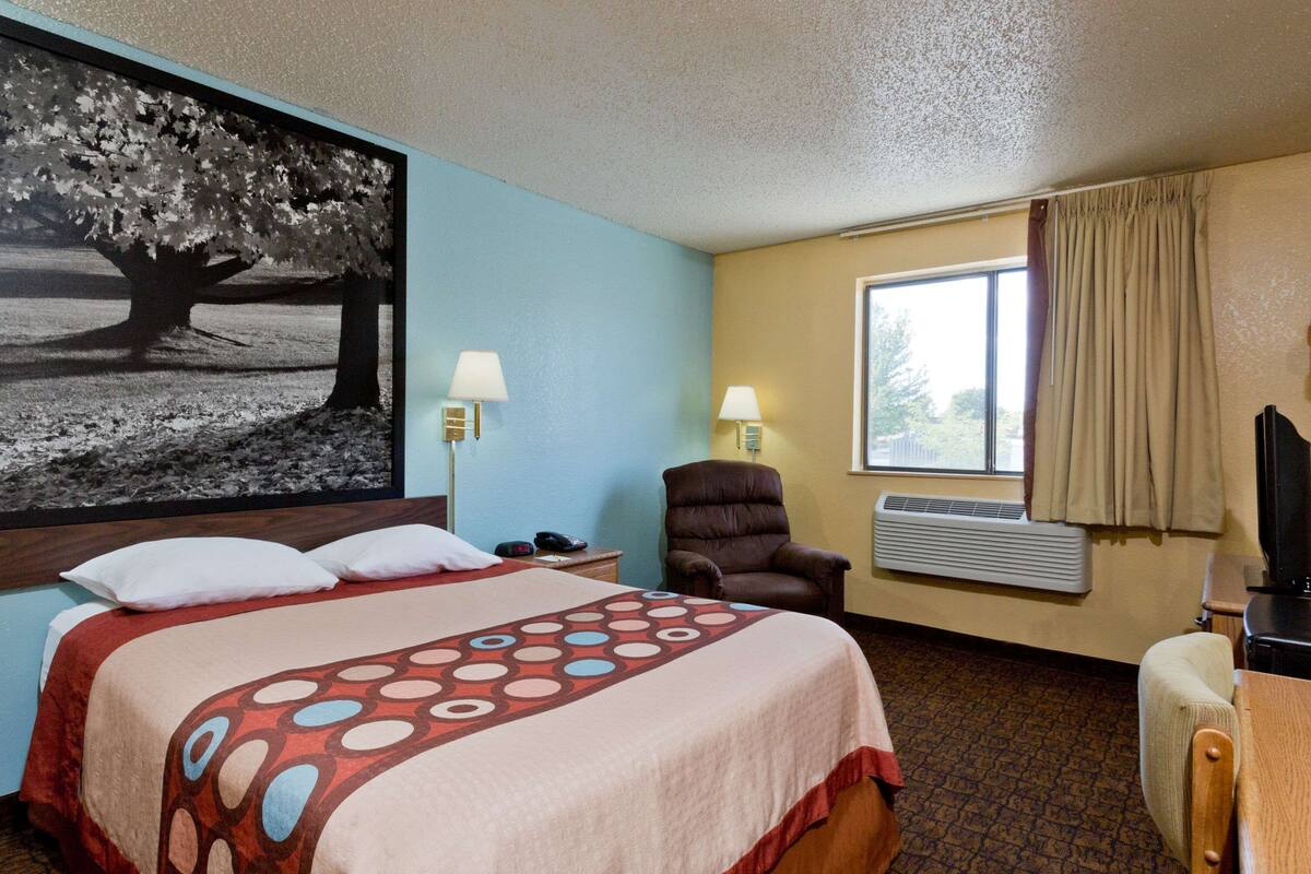 A hotel room with a bed, a chair, a desk, a lamp, a television, and a window with curtains.
