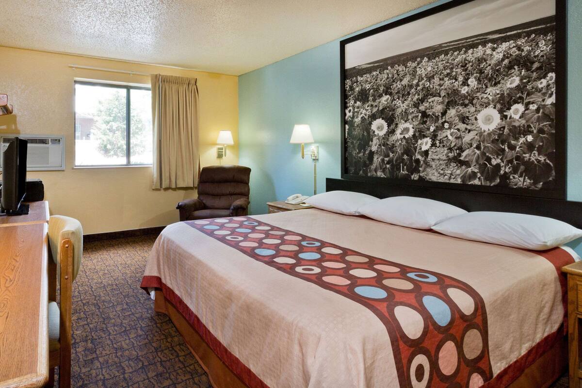 A hotel room with a bed, a desk, a chair, a window, and a wall-mounted lamp.