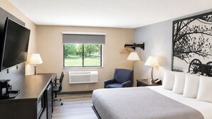 Une chambre d’hôtel équipée d’un lit, d’un bureau, d’une chaise, d’une télévision et d’œuvres d’art.