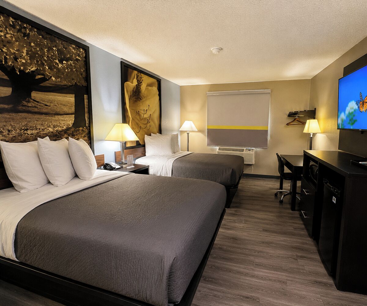 A hotel room with two beds, a desk, a TV, and a painting on the wall.