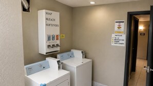 Ein Hotel-Waschraum mit zwei Whirlpool Waschmaschinen und Trocknern, einem Spender für Waschmittel und Bleichmittel sowie einem Schild, das die erste Etage und den Gemeinschaftswaschbereich kennzeichnet.