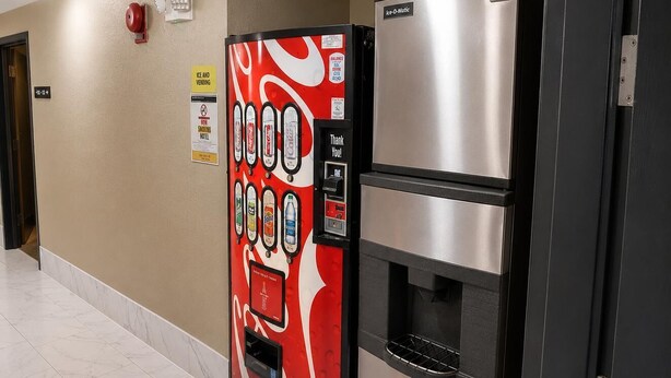 Un distributeur automatique orné du logo Coca-Cola, une fontaine à eau et un réfrigérateur, le tout installé dans un couloir.