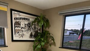 Ein Zimmer mit zwei Sesseln, einer großen Topfpflanze, einer gerahmten Karte von Kalifornien und einem großen Fenster.