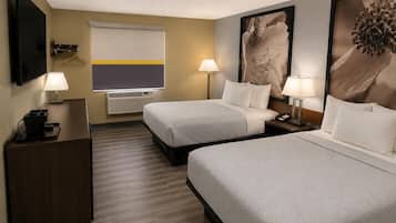 Habitación de hotel con dos camas, un escritorio con lámpara, televisión y obras de arte en las paredes.