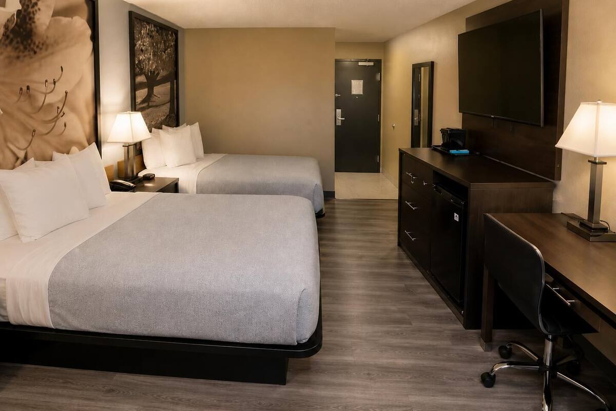 Habitació d'hotel amb dos llits, un escriptori, una cadira, un televisor i un aparador.
