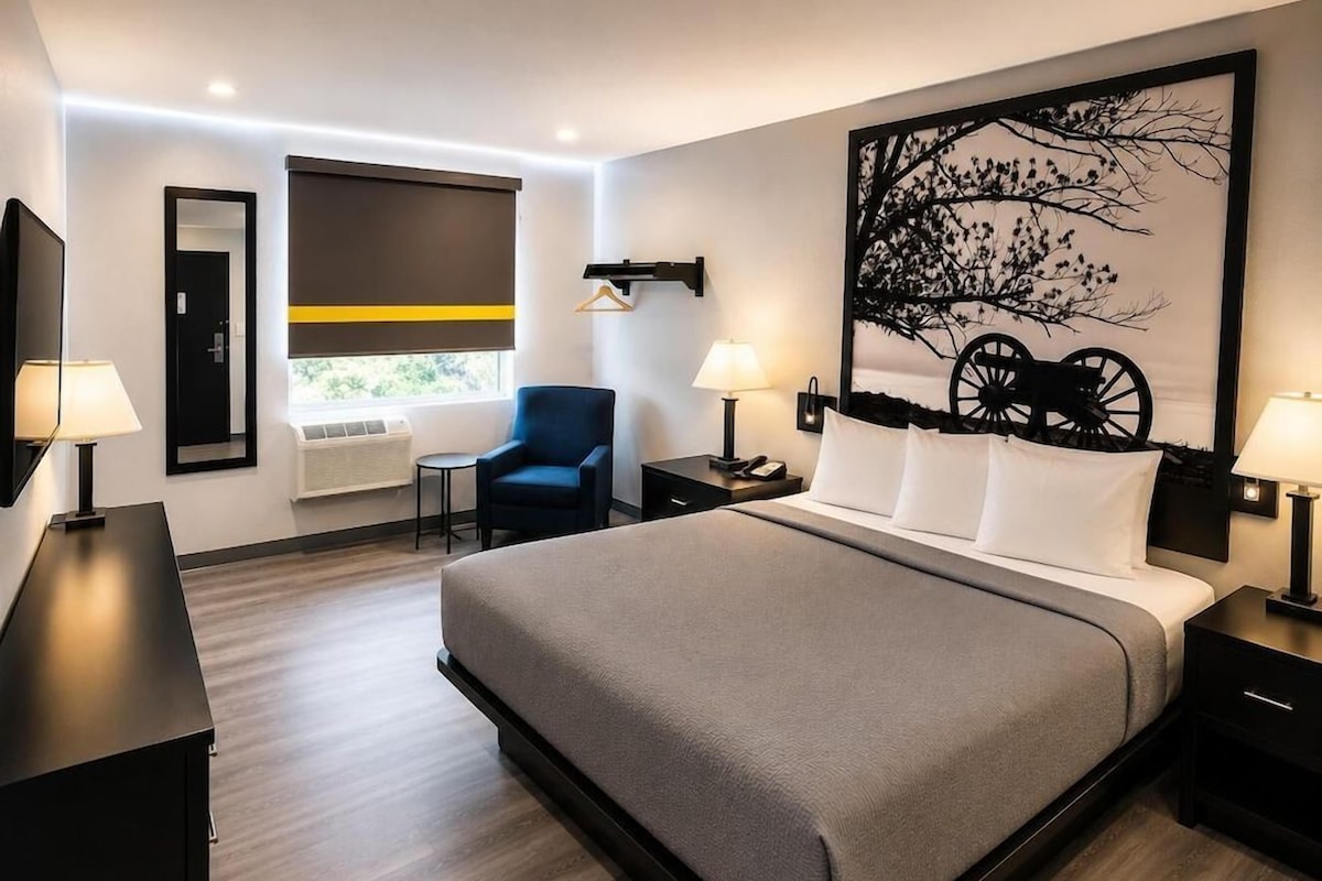 Une chambre d’hôtel moderne avec un grand lit, un bureau, une chaise et une fenêtre équipée de stores.