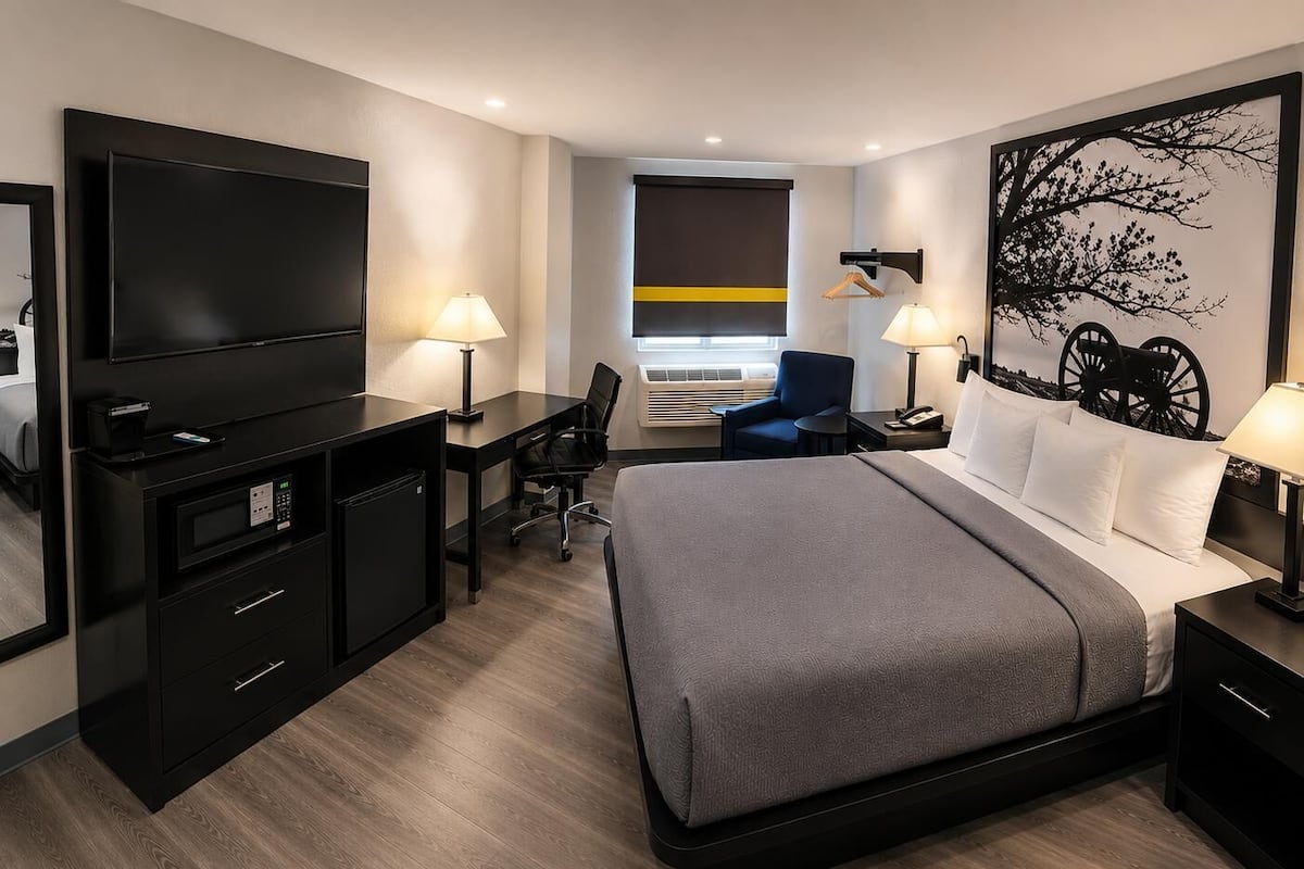 Habitació d'hotel moderna amb un llit gran, una taula de treball, una cadira, un televisor i aire condicionat fixat a la paret.