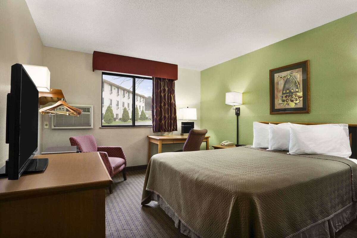 A hotel room with a bed, desk, chair, and a window with curtains.
