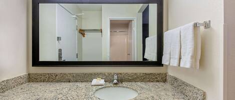 Une salle de bain avec un comptoir en granit, un lavabo blanc, un grand miroir et un porte-serviettes avec des serviettes blanches.