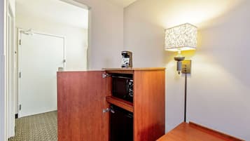 Habitación de hotel con un armario de madera, microondas, cafetera y una lámpara.