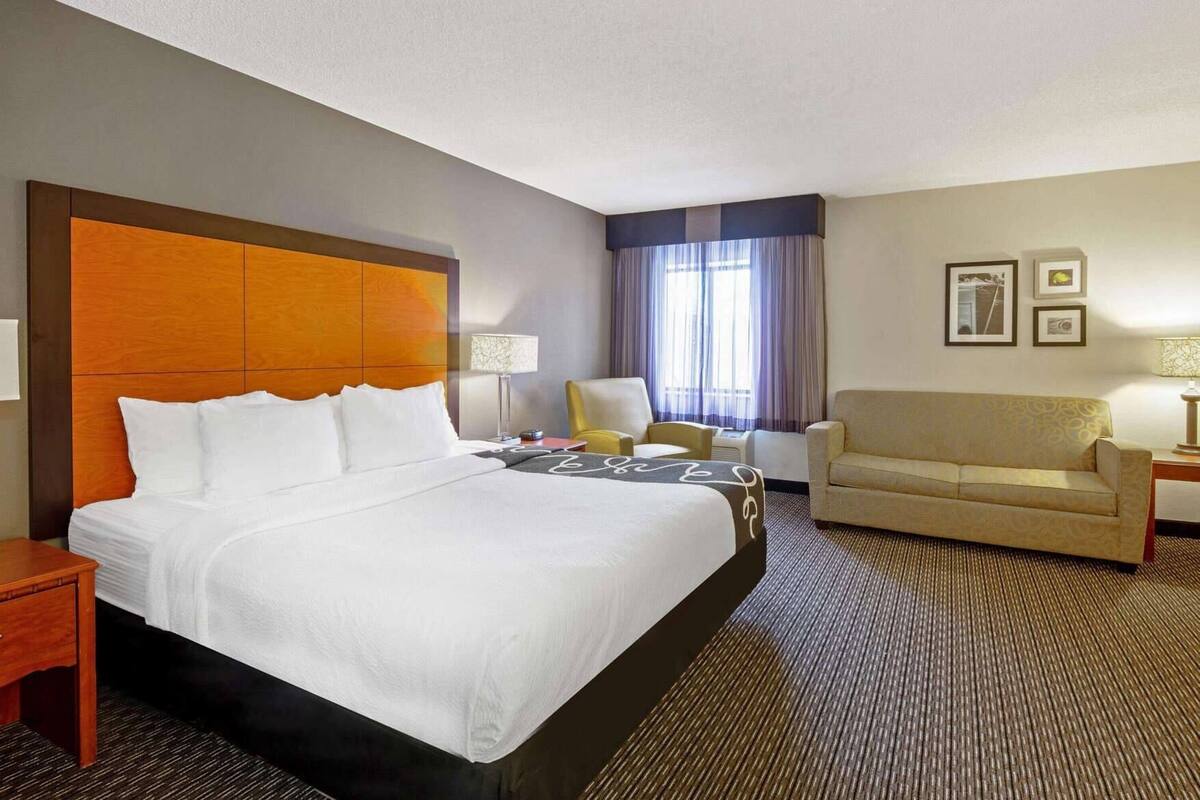 Ein Hotelzimmer mit einem großen Bett, einem Sofa, einem Sessel, einem Schreibtisch und einem Fenster mit Vorhängen.