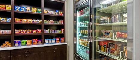 A snack and beverage refrigerator stocked with various items including chips, cereals, and bottled drinks.