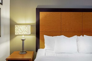 A neatly made bed with white linens, a wooden headboard, and a table lamp with a patterned shade. - La Quinta Inn & Suites by Wyndham Harrisburg Airport Hershey (Harrisburg)