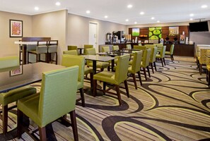 A hotel dining area with multiple tables and chairs, a coffee station, and a reception desk. - La Quinta Inn & Suites by Wyndham Harrisburg Airport Hershey (Harrisburg)