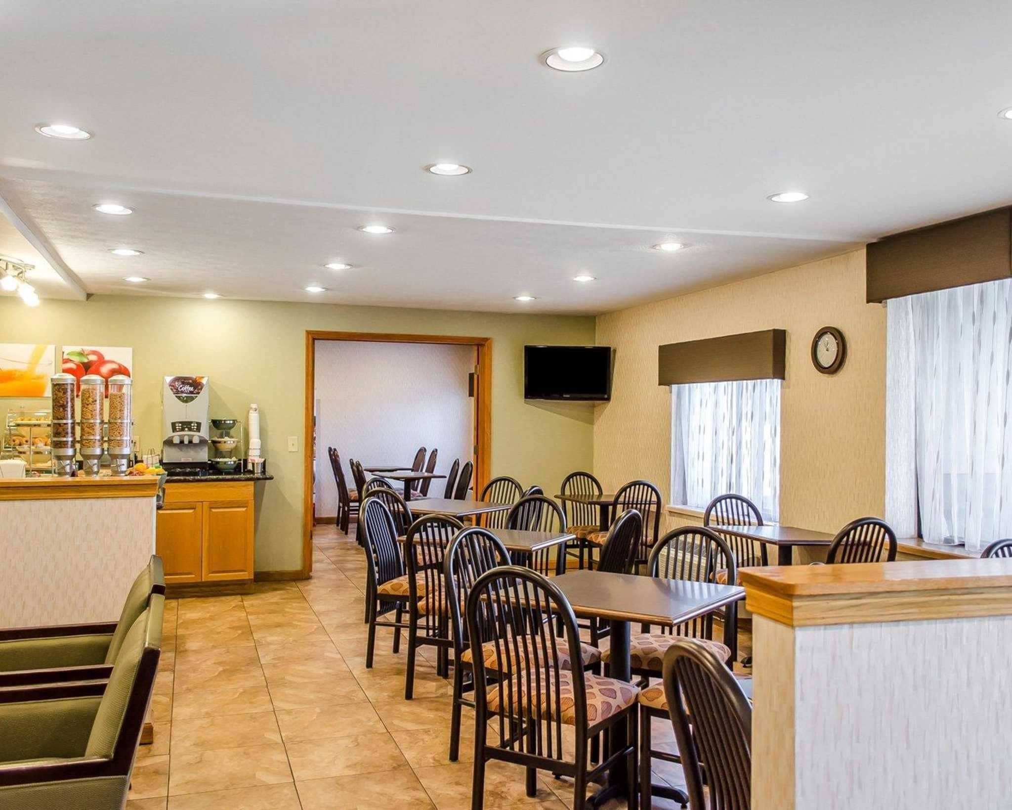 A hotel dining area with multiple tables and chairs, a coffee station, and a television mounted on the wall.