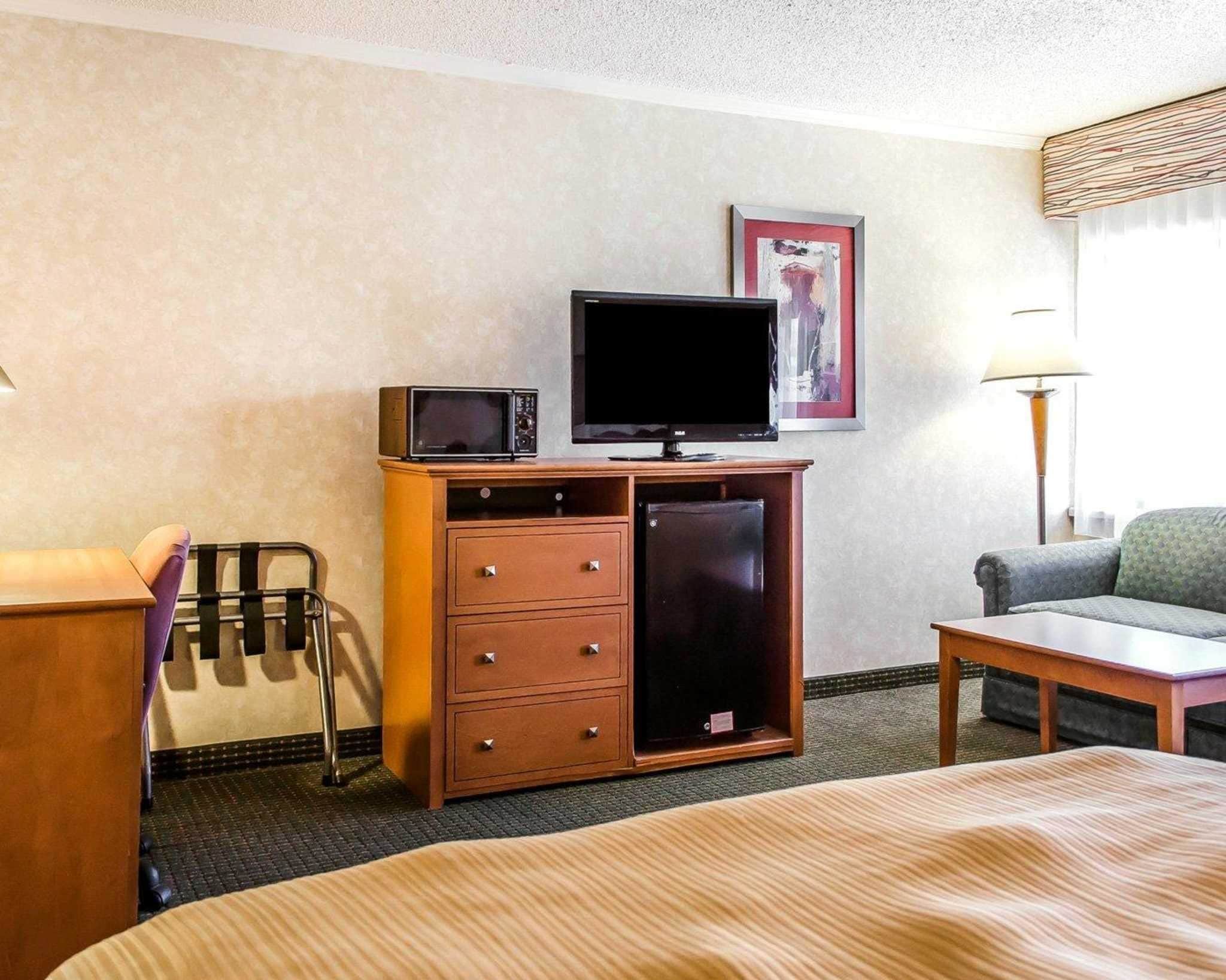 A hotel room with a bed, a wooden dresser with a television and microwave, a chair, and a lamp.