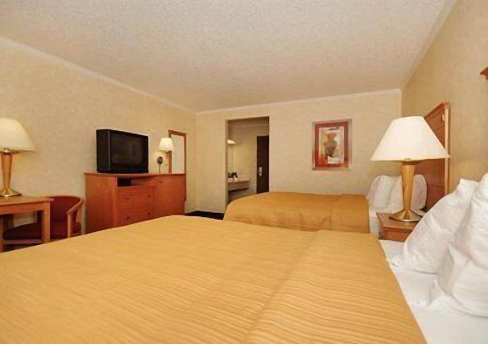 Una habitación de hotel con dos camas, un televisor, un escritorio y una lámpara.