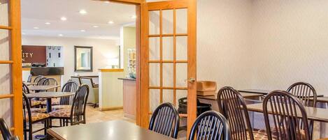 A dining area with tables and chairs, a wooden door, and a kitchen in the background.