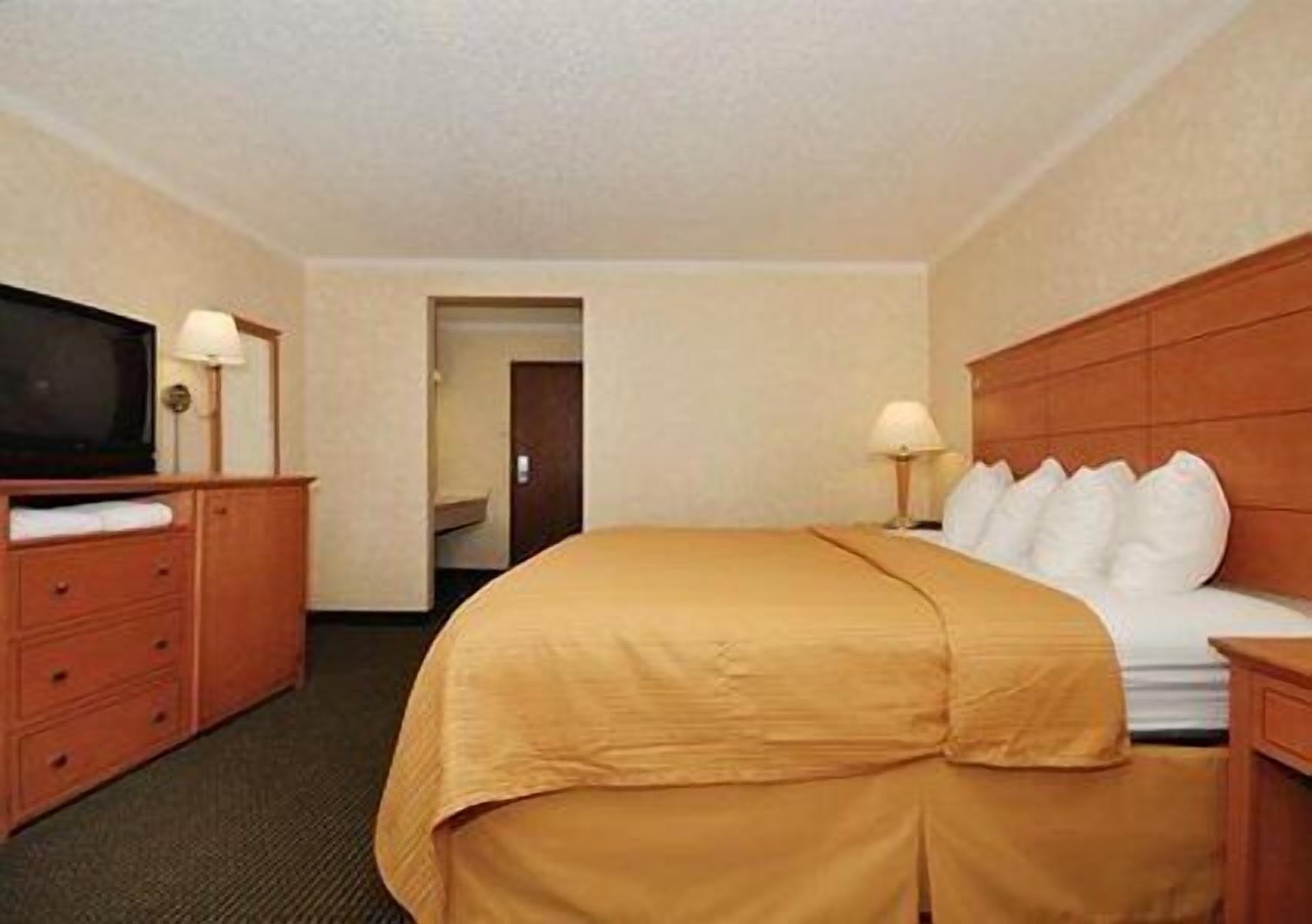 Una habitación de hotel con cama, televisor, cómoda y una puerta que da a otra habitación.