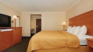 Una habitación de hotel con cama, televisor, cómoda y una puerta que da a otra habitación.