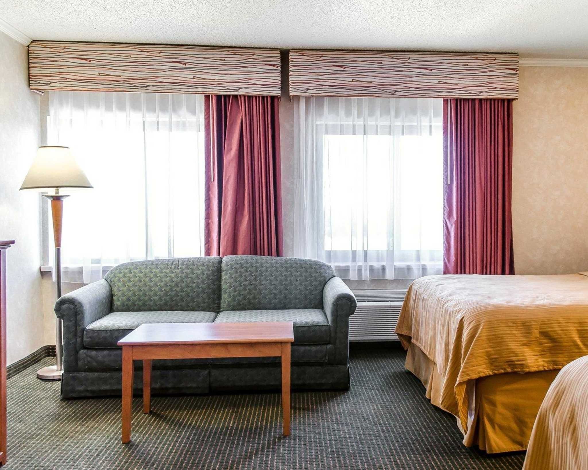 Una habitación de hotel con sofá, una mesita, cama y ventana con cortinas.