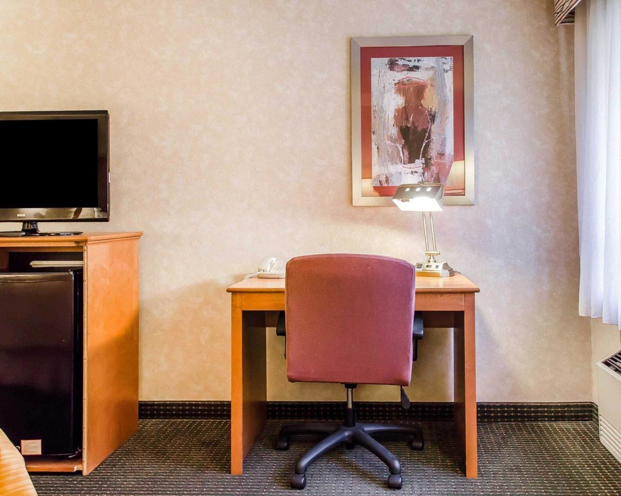 A hotel room with a desk, chair, television, and a framed artwork on the wall.
