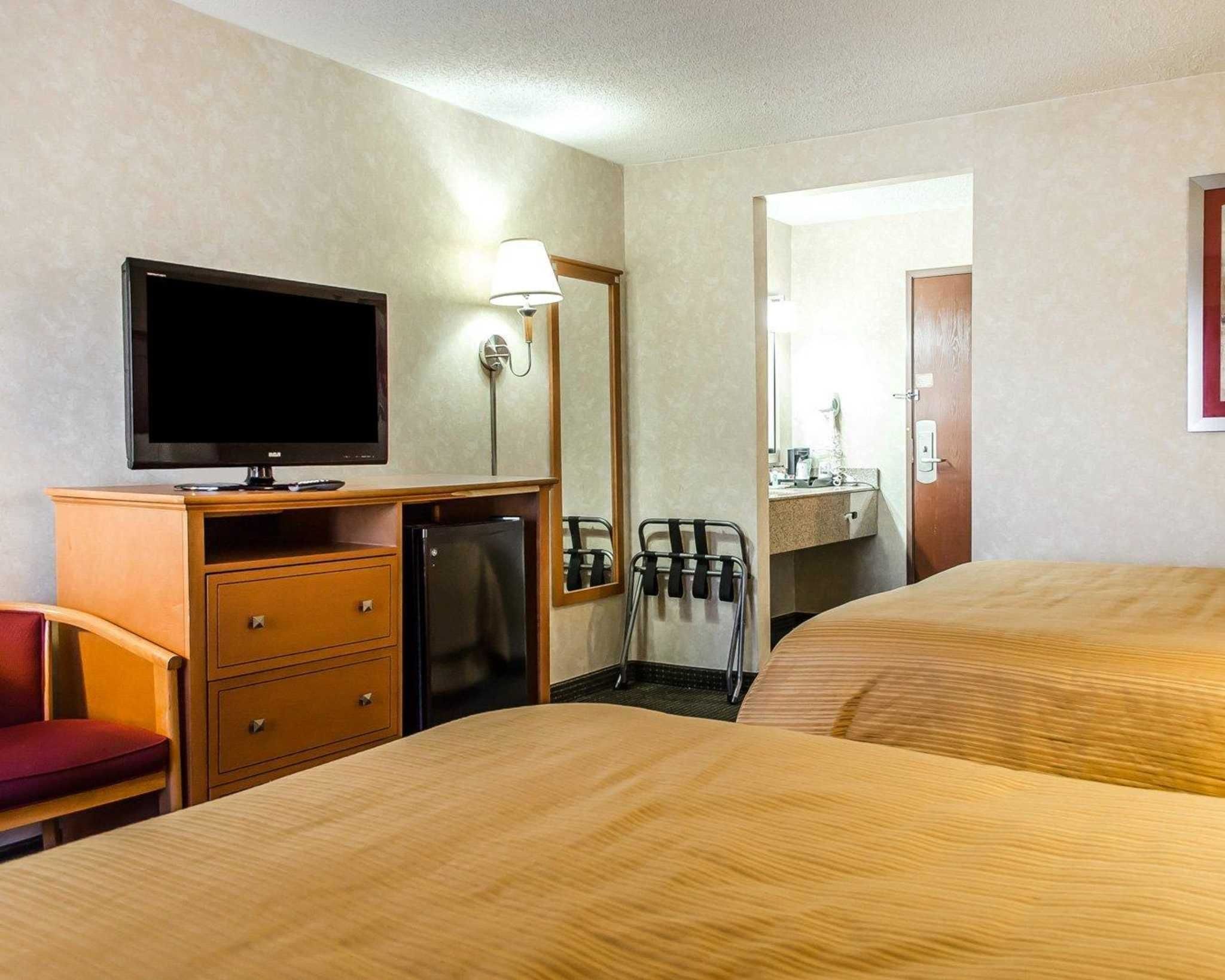 A hotel room with two beds, a TV, a desk with a lamp, a mirror, and a door leading to a bathroom.