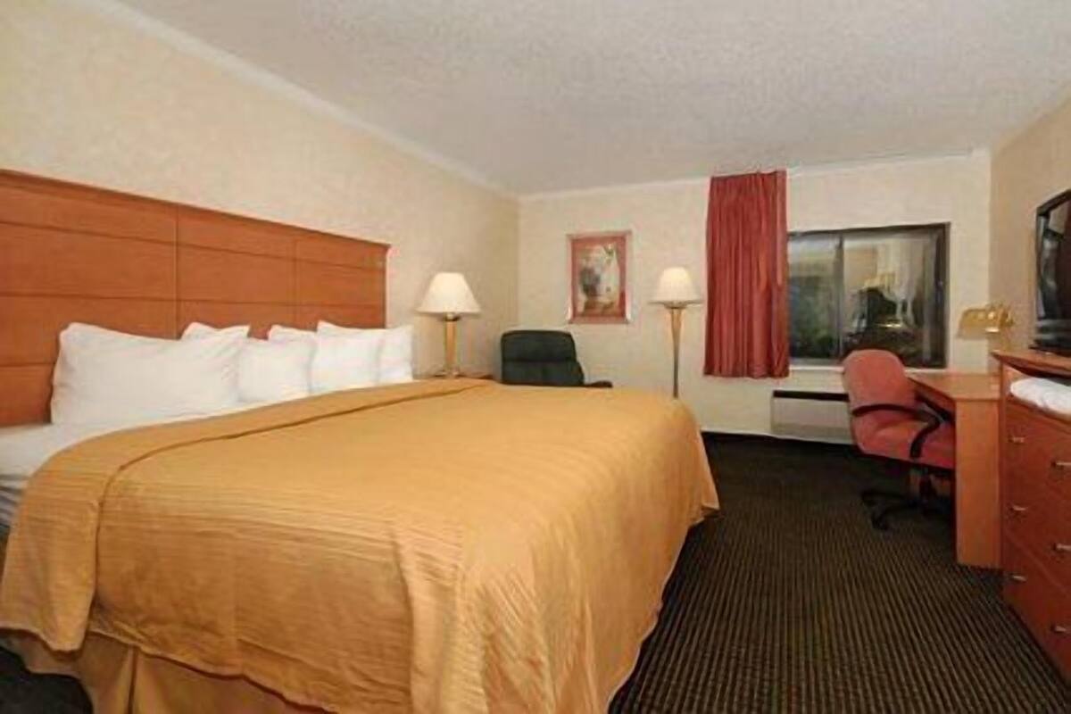 A hotel room with a large bed, a desk, a chair, and a television.