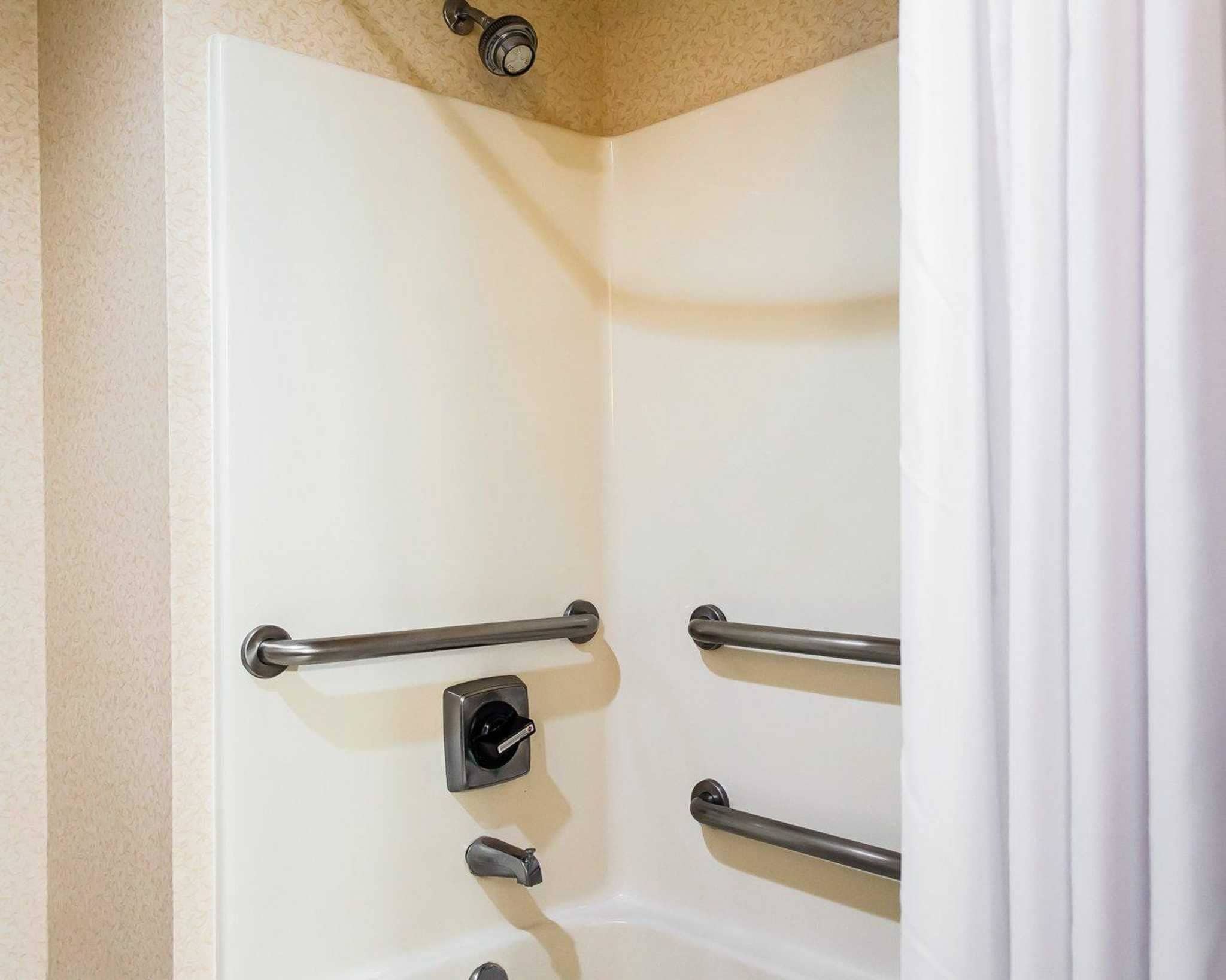 A shower with a white door, a handheld showerhead, and two grab bars.