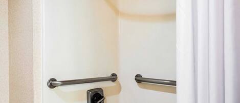 A shower with a white door, a handheld showerhead, and two grab bars.