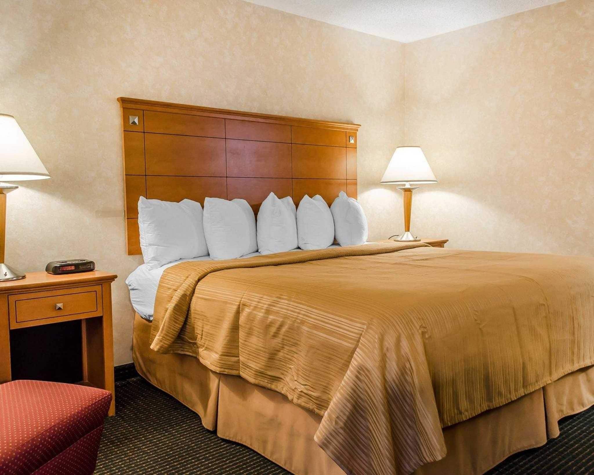 A hotel room with a large bed, two bedside tables, a wooden headboard, and two lamps.