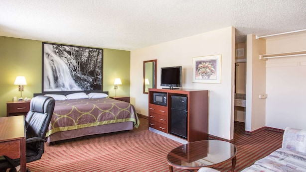 A hotel room with a bed, a desk, a chair, a TV, a microwave, a dresser, and a painting on the wall. - Super 8 by Wyndham Harrisonburg (Harrisonburg)