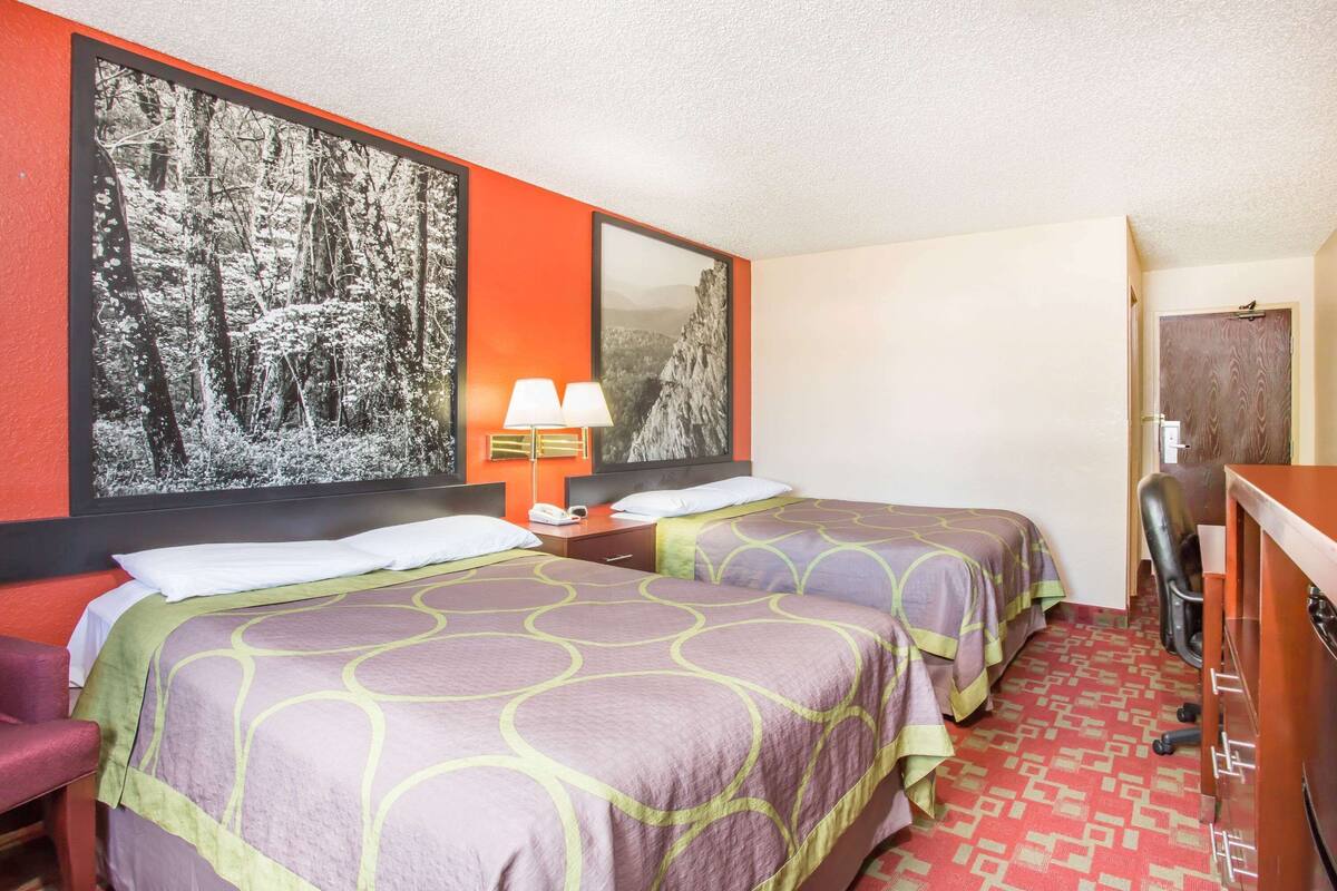 Une chambre d’hôtel avec deux lits, un bureau, une chaise et un grand tableau encadré au mur.