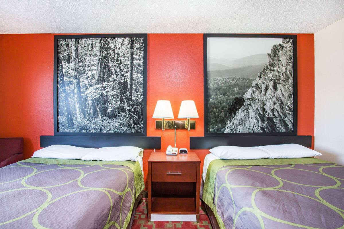 Une chambre d’hôtel avec deux lits, une table de chevet avec des lampes et deux grandes images encadrées au mur.