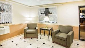 A room with two armchairs, a small table with a lamp, and a window with lace curtains. - Super 8 by Wyndham Harrisonburg (Harrisonburg)