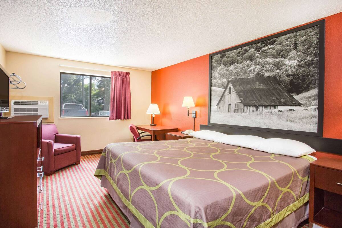 Une chambre d’hôtel avec un grand lit, un bureau, une chaise, une fenêtre avec des rideaux et un climatiseur fixé au mur.