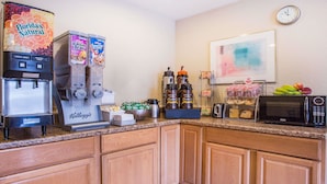 A kitchen with a coffee machine, a fruit dispenser, a microwave, and a clock on the wall. - Super 8 by Wyndham Harrisonburg (Harrisonburg)