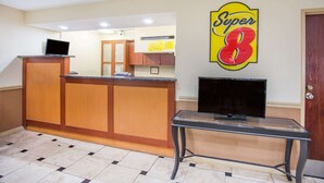 A reception area with a wooden counter, a glass table with a TV, and a 'Super 8' sign on the wall. - Super 8 by Wyndham Harrisonburg (Harrisonburg)