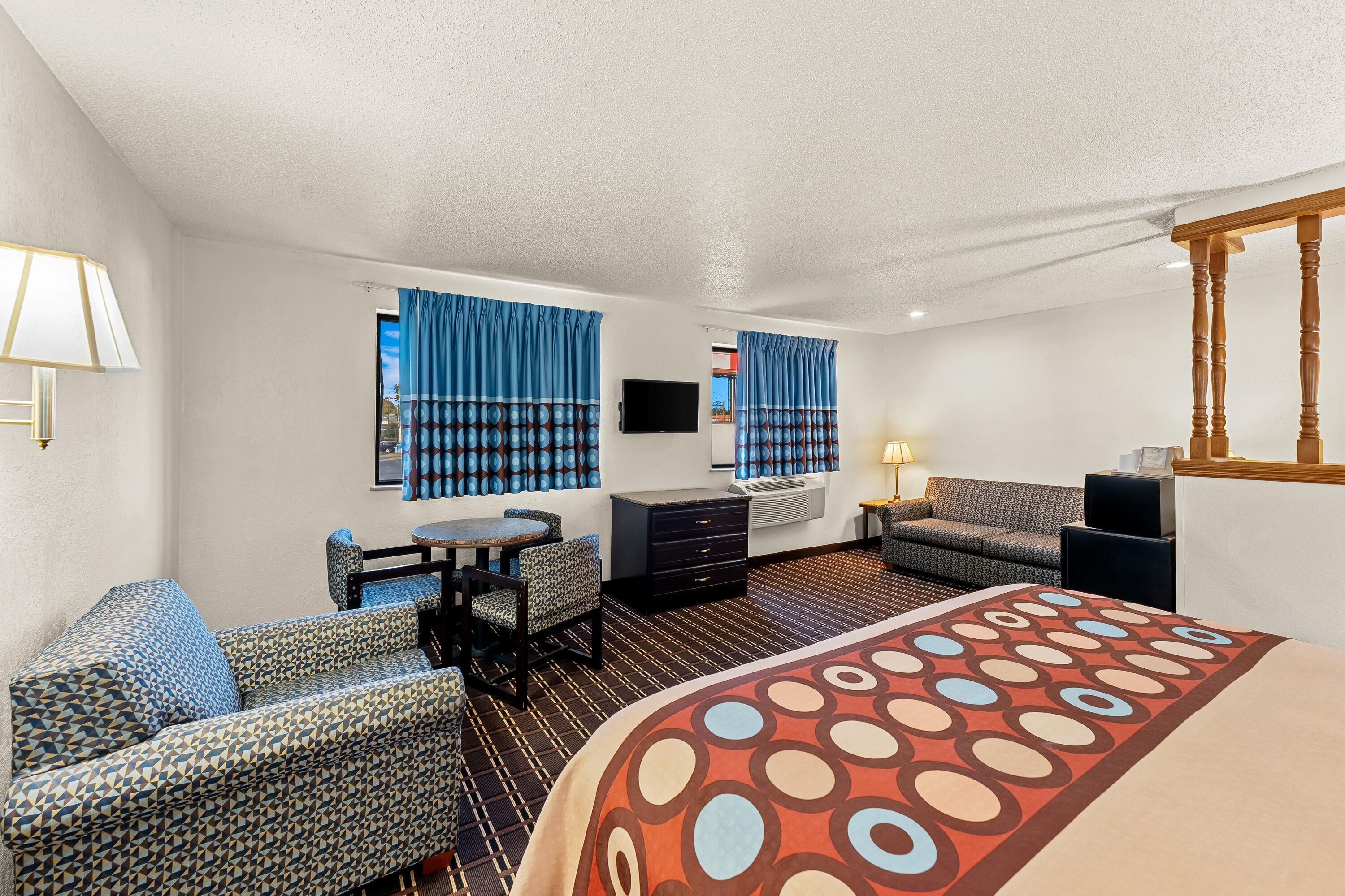 A hotel room with a bed, a desk, a chair, a sofa, a TV, and a window with curtains.
