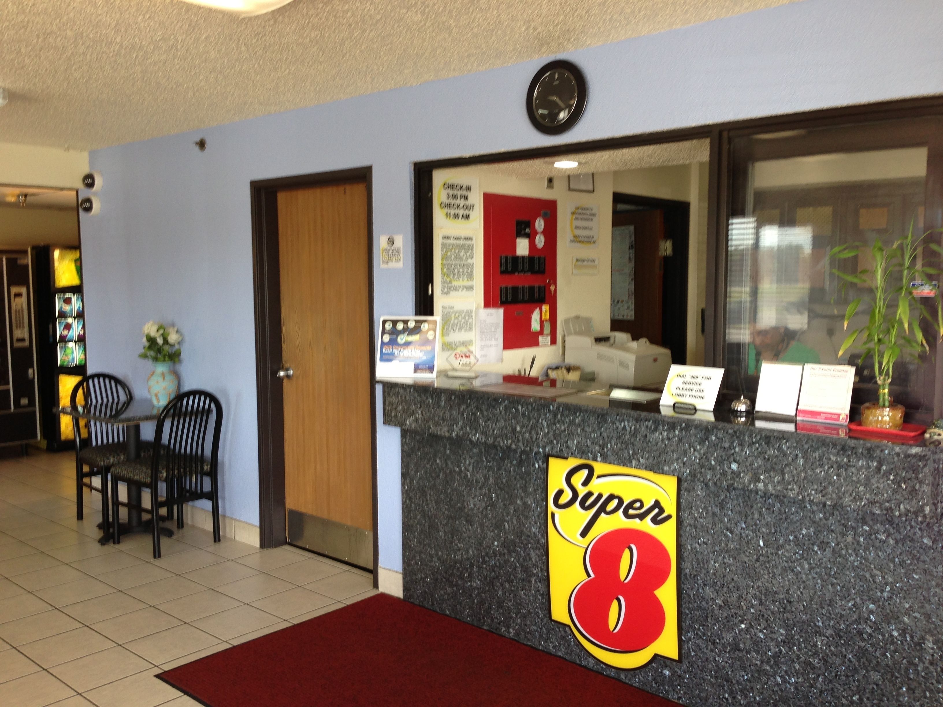 Un comptoir d’accueil avec une enseigne « Super 8 », une horloge et un mur rouge avec une porte.